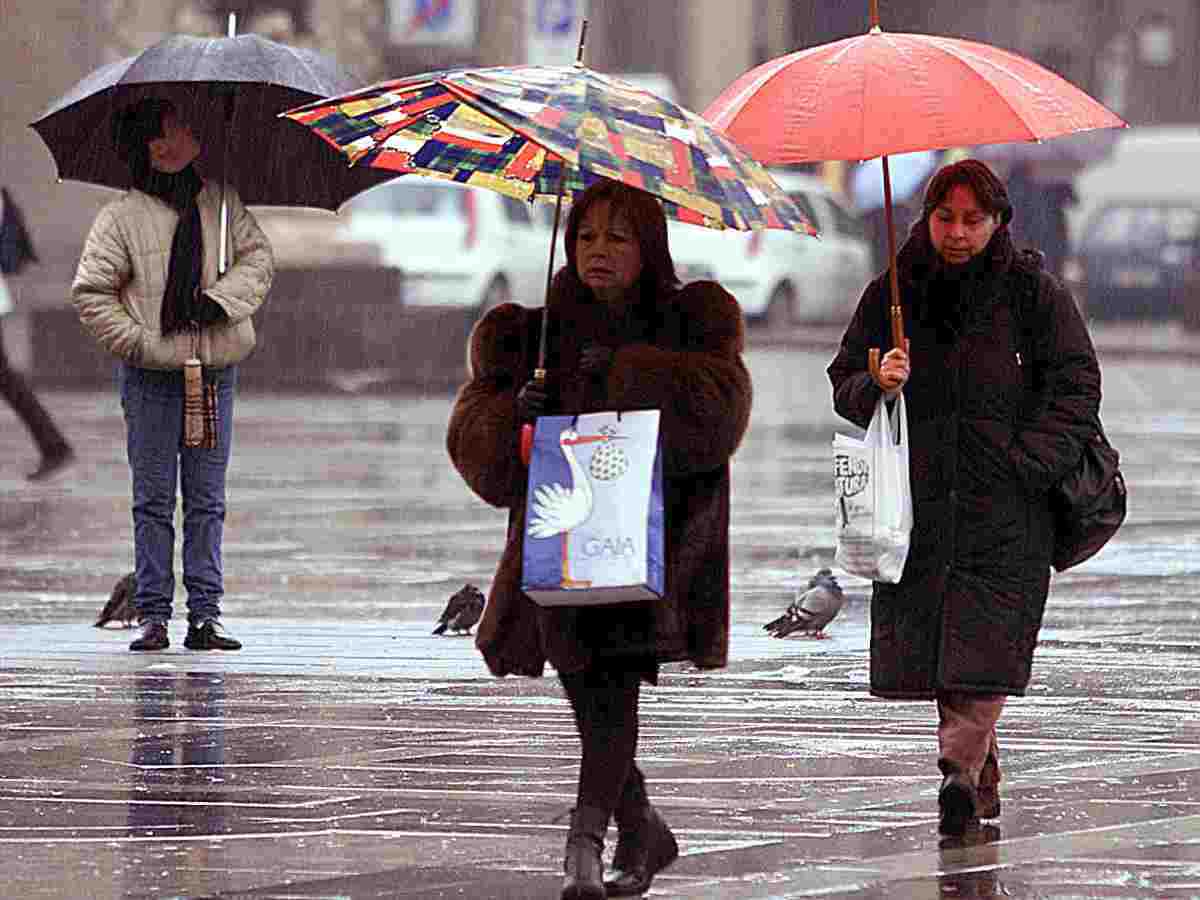 Signore che passeggiano sotto la pioggia con ombrello aperto