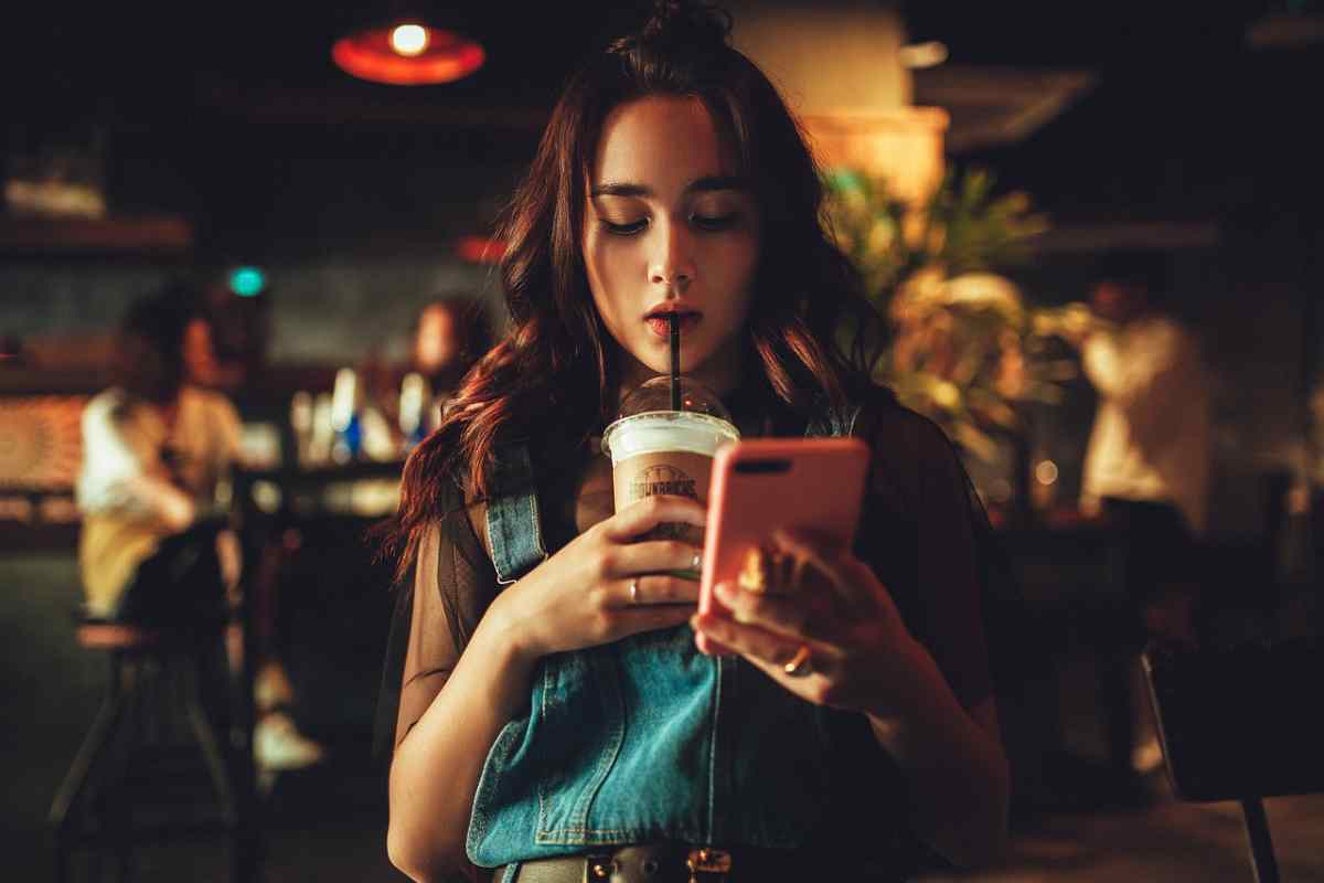 ragazza che osserva il suo telefono e beve